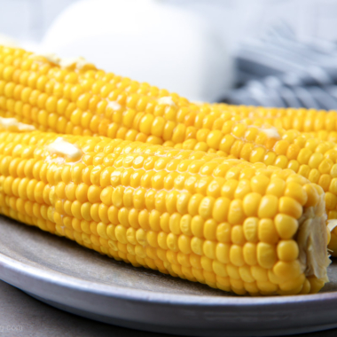 Microwave corn on the cob on a white plate with butter melting on top.
