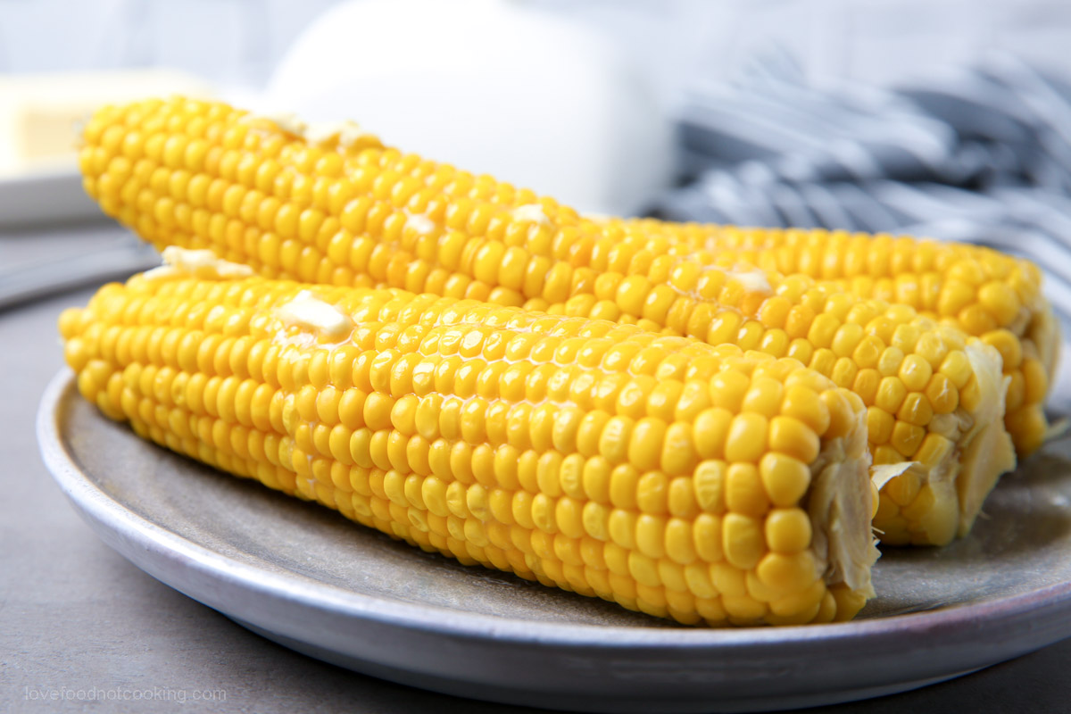 Microwave corn on the cob on a white plate with butter melting on top. 