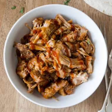 Slow cooker pulled pork in a white bowl.