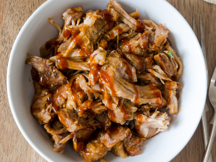 Slow cooker pulled pork in a white bowl.