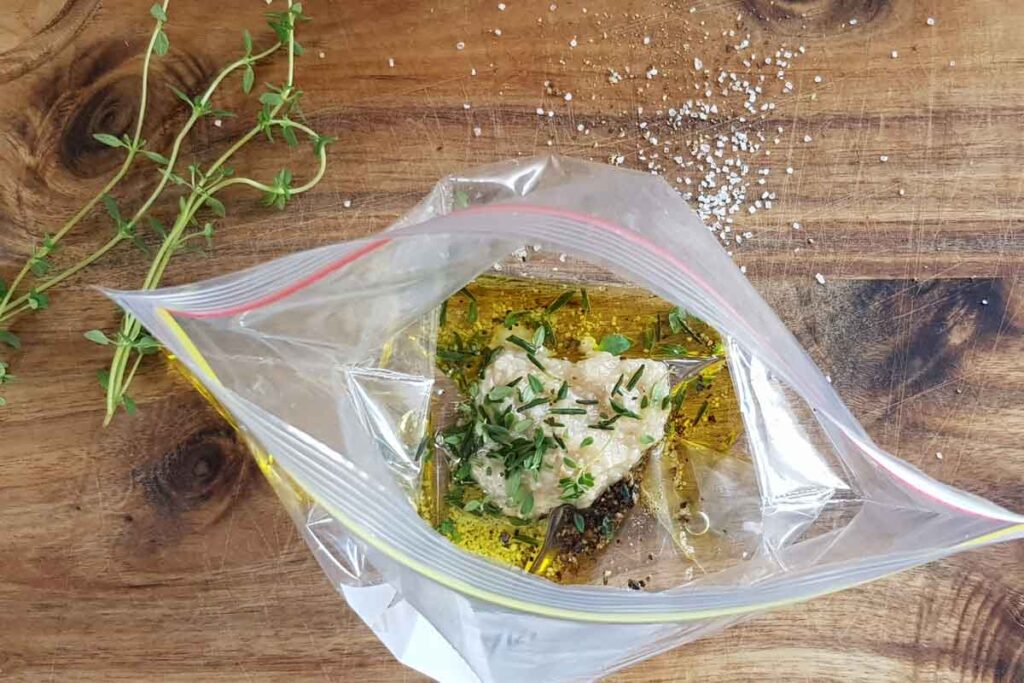an open zip-lock bag with oil, garlic and herbs inside. 