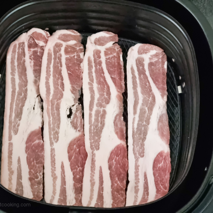 Raw bacon in air fryer basket. 
