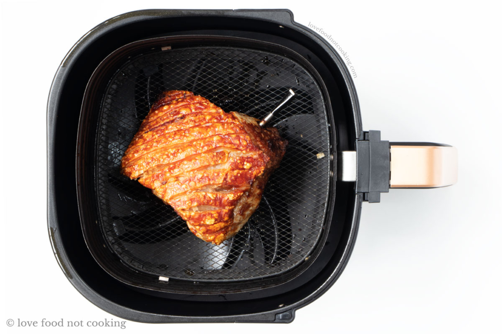 Cooked pork roast in air fryer basket with perfect golden brown crackling.