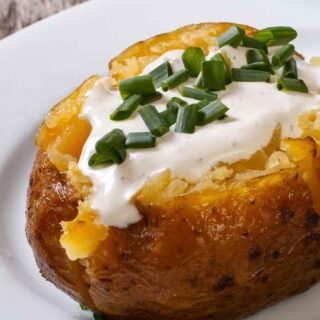 Air fryer baked potato with sour cream and chives on a white plate