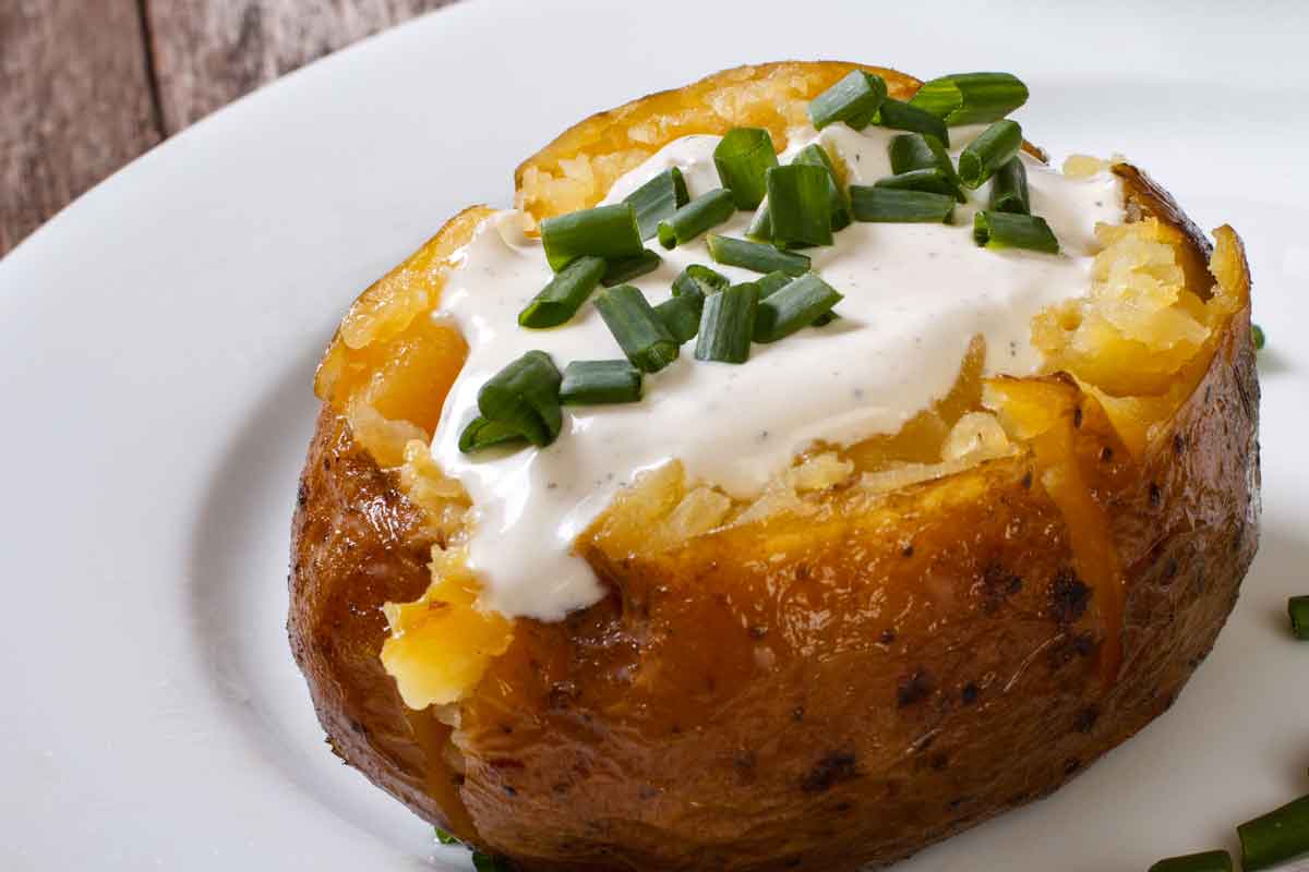 Air fryer baked potato with sour cream and chives on a white plate