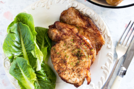 Air fryer pork chops with salad on a white plate.