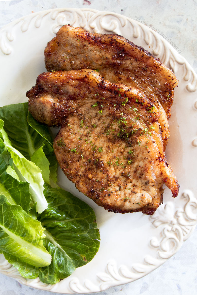 Vertical picture of air fryer pork chops with salad on a white plate.