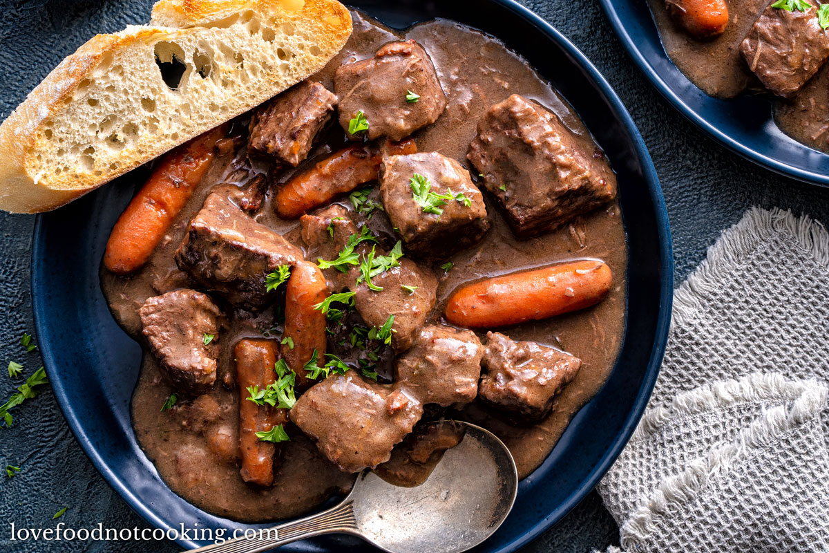 Slow cooker beef stew in a blue bowl with a slice of ciabatta bread.
