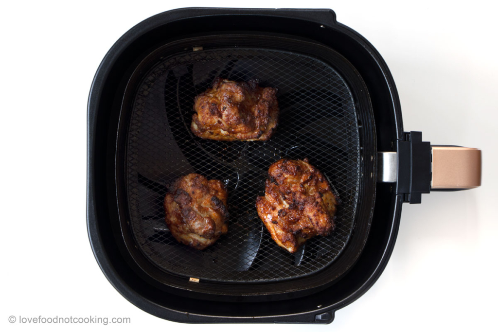 Cooked chicken thighs in air fryer basket.