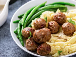 Air fryer meatballs on a white plate with green beans and potatoes.