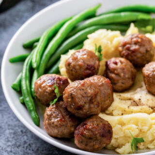 Air fryer meatballs on a white plate with green beans and potatoes.
