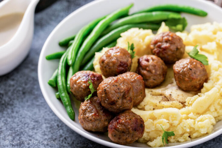 Air fryer meatballs on a white plate with green beans and potatoes.