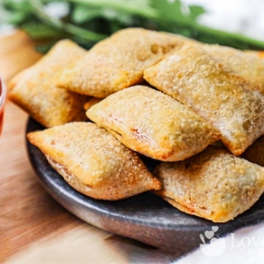 Air fried pizza rolls on a black plate with tomato sauce.