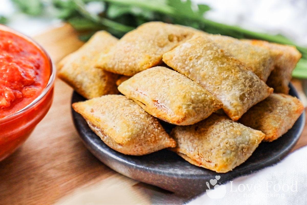 Air fryer pizza rolls on a black plate with tomato sauce.