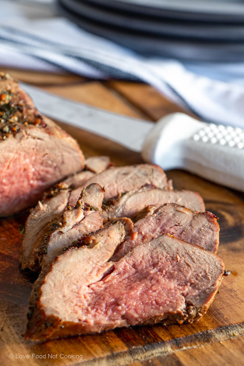 Air fryer lamb roast on a wooden board with carving knife.