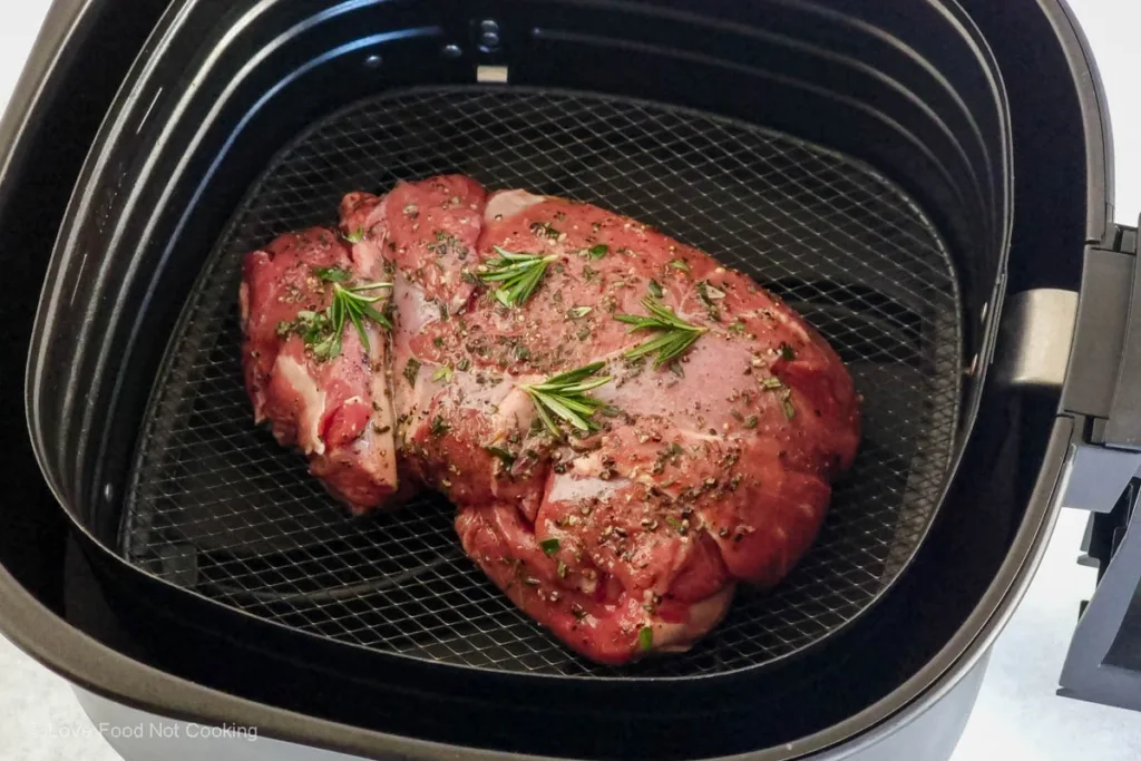 Uncooked roast lamb in air fryer basket. 