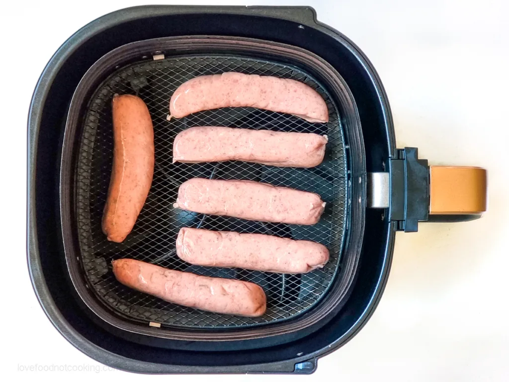 Uncooked sausages in air fryer basket.