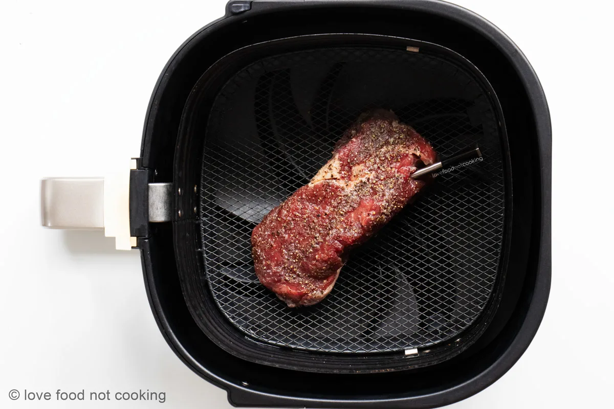 Uncooked steak in air fryer basket. 