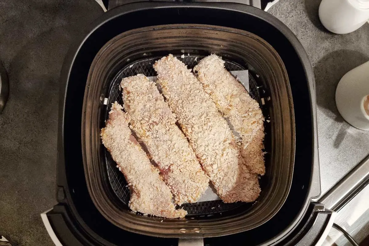 Uncooked tilapia fillets in the air fryer basket. 