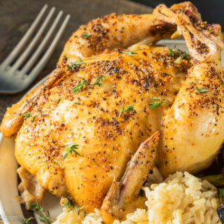 Air fryer Cornish hen on a white plate with rice and broccoli.