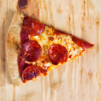 Reheated leftover pepperoni pizza slice on a wooden board.