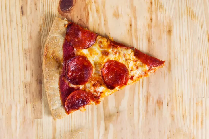 Reheated leftover pepperoni pizza slice on a wooden board.