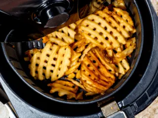 Crispy waffle fries in air fryer basket.