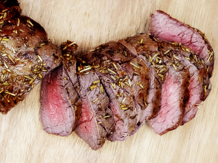 Sliced air fryer beef tenderloin on a wooden board.