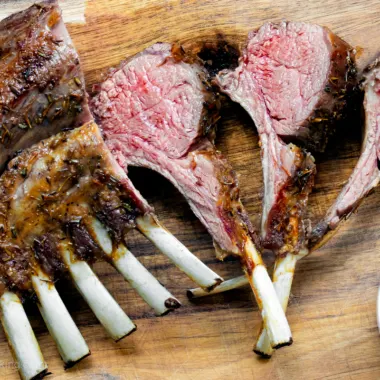 Air fryer rack of lamb on a wooden board with mint sauce.