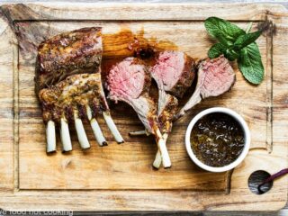 Air fryer rack of lamb on a wooden board with mint leaves and sauce