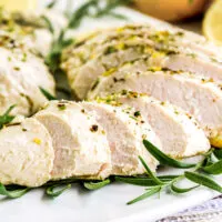 Instant Pot turkey tenderloin on a white plate with lemon slices and herbs.
