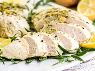 Instant Pot turkey tenderloin on a white plate with lemon slices and herbs.