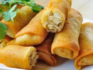 A pile of egg rolls on a white plate.