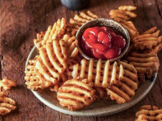 Waffle fries on a white plate with tomato sauce.