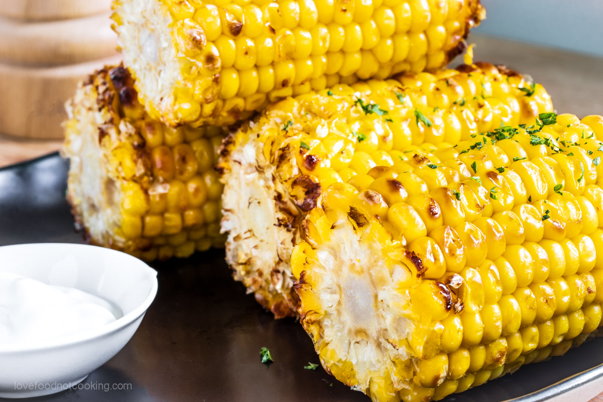 Air fried corn cobs on a black plate with dip.
