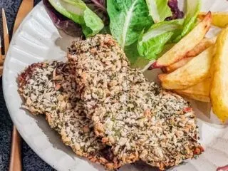 Air fryer beef schnitzel with fries and salad on a cream plate.