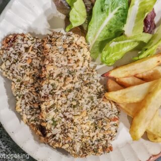 Air fryer beef schnitzel with fries and salad on a cream plate.