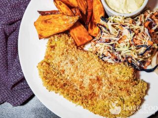 Air fryer pork schnitzel on a white plate with slaw and sweet potato fries.