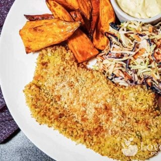 Air fryer pork schnitzel on a white plate with slaw and sweet potato fries.