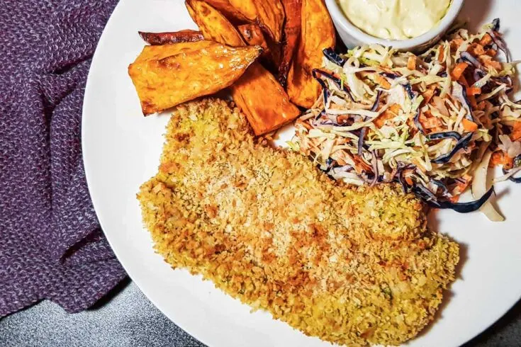 Air fryer pork schnitzel on a white plate with slaw and sweet potato fries.