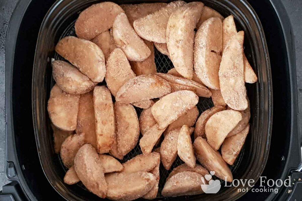 Cunei di patate surgelati nel cestino della friggitrice ad aria.