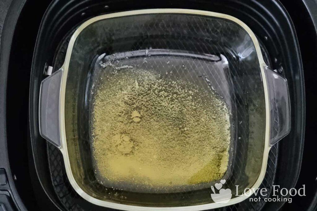 Melted butter in a baking dish inside an air fryer basket. 