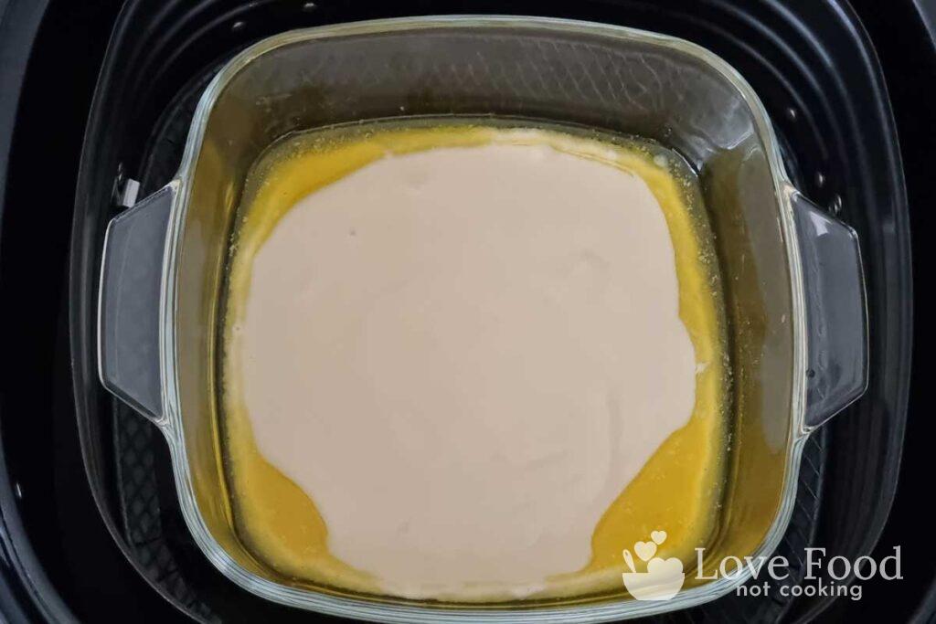 Melted butter and uncooked batter in a baking dish in an air fryer basket. 