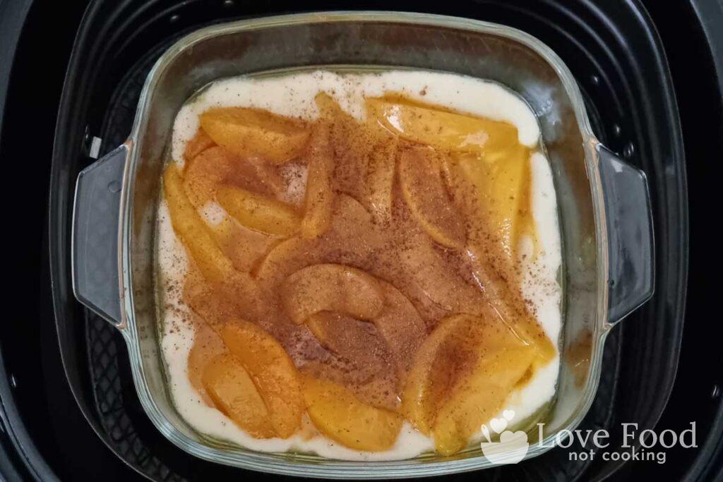Peach slices and cinnamon ontop of batter and melted butter in an air fryer basket. 