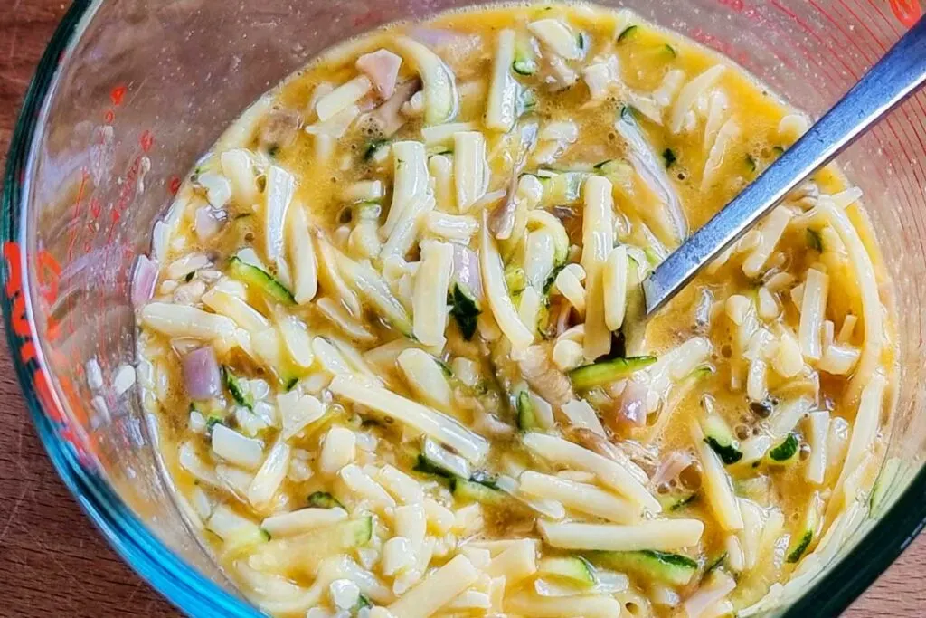 A mwasuring jug with egg, shredded cheese, diced ham and grated zucchini mixed together. 