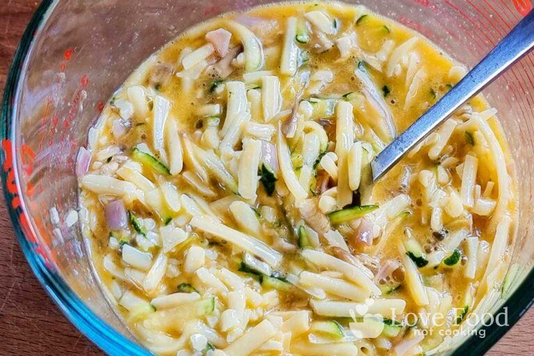 A mwasuring jug with egg, shredded cheese, diced ham and grated zucchini mixed together. 