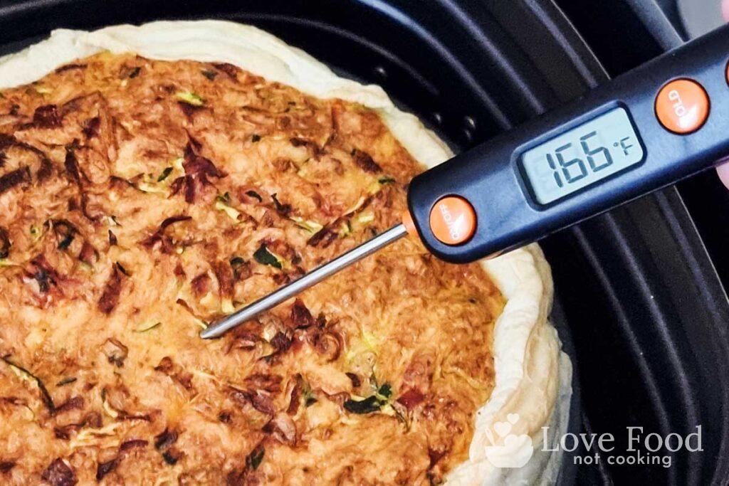 Cooked quiche in air fryer basket, with instant-read thermometer reading 160F. 