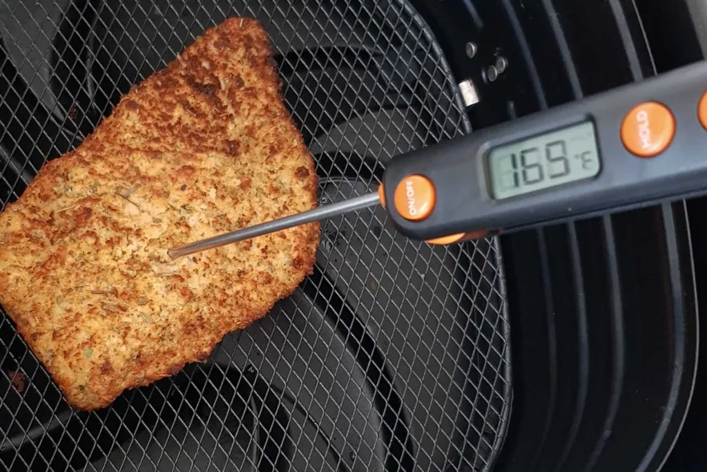 Cooked chicken schnitzel in air fryer basket with instant-read meat thermometer - 169F.