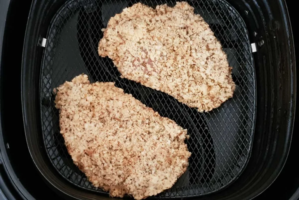 Prepared chicken schnitzels in air fryer basket.