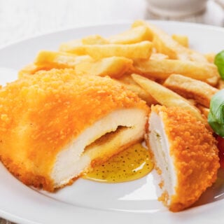 Air fryer frozen chicken kiev on a white plate with fries and salad.